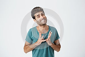 Close up portrait of funny stylish spanish guy in blue tshirt, biting lips and gesticulating with hands expressing