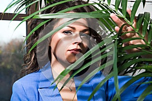 Close up. Portrait of a girl in a blue suit, the shadow of the leaves of a green tropical plant falls on her face