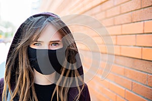 Close-up portrait of girl with dreadlocks and green-blue eyes, wearing medical flu mask and hooded sweater, looking straight, on