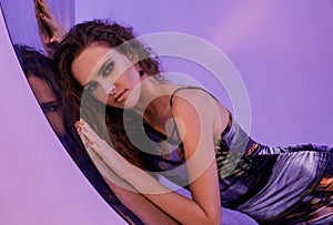 Close-up portrait. Girl lean on onto a reflective surface at the neon background