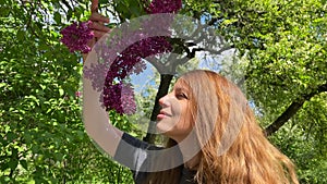 Close-up portrait of a girl sniffing a burgundy lilac in a botanical garden.