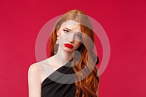 Close-up portrait of gloomy and upset young redhead woman in red lip gloss, black evening dress, want to cry but have