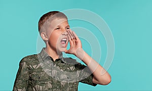 Close-up portrait of a blonde teenage boy in a green shirt with palm print posing against a blue studio background