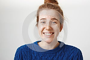 Close-up portrait of good-looking girl with freckles and natural red hair smiling nervously and chuckling, talking with