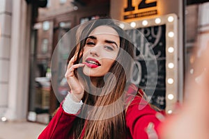 Close-up portrait of good-looking woman with dark hair making selfie on blur city background. Outdoor photo of sensual