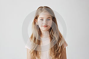 Close up portrait of good-looking young girl with blond hair in pink dress, looking in camera with calm expression