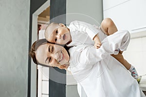 Close up portrait of good-looking young mother holding little son on her back smiling, playing and spending great time