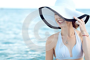 Close up portrait of gorgeous glam smiling lady hiding the half of her face behind the wide brim hat