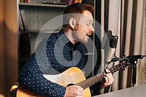 Close-up portrait of guitarist singer man play on acoustic guitar recording sing song using professional microphone