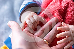 A close up portrait of the hand of a father being held by the small baby hands of his child. The little cute fingers are rapped