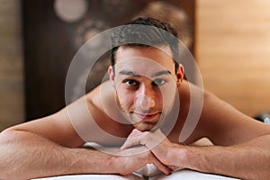 Close-up portrait of handsome bearded man lying on massage table and smiling looking at camera in wellness center