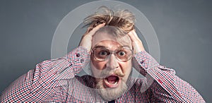 Close-up portrait of a handsome bearded young guy with a surprised face and tousled hair wearing very large glasses.