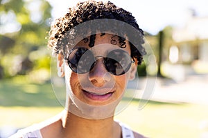 Close-up portrait of handsome biracial young man wearing sunglasses and posing in yard