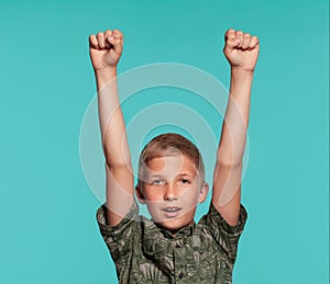 Close-up portrait of a blonde teenage boy in a green shirt with palm print posing against a blue studio background