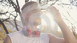 Close-up portrait of handsome Caucasian athletic man drinking water in sunlight. Young sportive boy training outdoors on