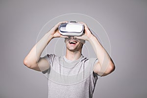 Close up portrait of handsome male in grey t-shirt, experiencing virtual reality using VR headset glasses. Young man wearing goggl