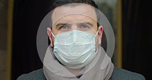 Close up portrait of handsome male in medical mask standing outdoors on street and looking at camera. Caucasian serious