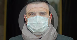 Close up portrait of handsome male in medical mask standing outdoors on street and looking at camera. Caucasian serious