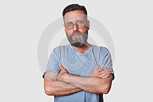 Close up portrait of handsome man with beard standing with arms folded isolated on white background, looks serious, wearing casual