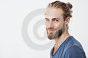 Close up portrait of handsome manly guy with beard posing in three quarters, looking in camera and happily smiling