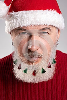 Close up portrait of handsome middle aged man with decorated beard wearing Christmas hat and red sweater looking at