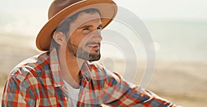 close up portrait of handsome stylish casual man traveler in hat sitting at sea coastline and enjoying peaceful nature