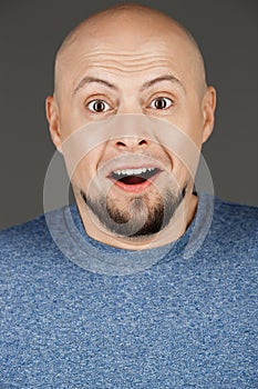 Close up portrait of handsome surprised middle-aged man in grey shirt over dark background.