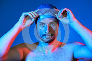 Close up portrait of handsome swimmer with goggles in red-pink neon light over blue background