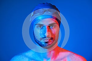 Close up portrait of handsome swimmer with goggles in red-pink neon light over blue background