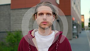 Close-up portrait of handsome young hipster man, guy standing outdoors street alone serious sad looking at camera