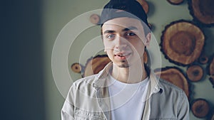 Close-up portrait of handsome young man wearing black cap, white T-shirt and beige shirt looking at camera and smiling