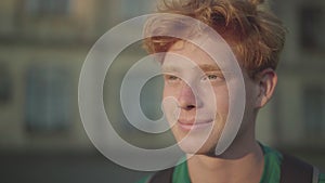 Close-up portrait of handsome young redhead man in sunlight. Smiling Caucasian guy enjoying sunny evening outdoors