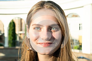 Close up portrait of the happy brunette girl with blue eyes and natural make up with sun rays on her face