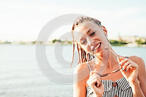 Close up portrait happy carefree young woman with african braids in sunglasses enjoy life on beach, summer vacation time