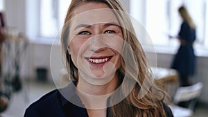 Close-up portrait of happy Caucasian blonde business woman posing at trendy modern office workplace, smiling cheerfully.