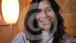 Close-up portrait of happy caucasian brunette woman watching into camera with sincere smile in cozy home atmosphere.