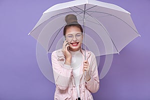 Close up of portrait of happy Caucasian woman holding white umbrella, having pleasant conversation over cell phone  over