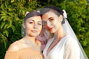 Close up portrait of happy charming bride in a white dress with white veil and a bridesmaid in a beige dress with pink