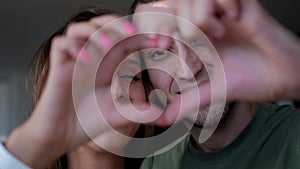 Close up portrait happy couple faces looking through joined fingers making heart shape. St Valentines Day celebration