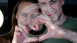 Close up portrait happy couple faces looking through joined fingers making heart shape. St Valentines Day celebration