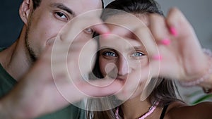 Close up portrait happy couple faces looking through joined fingers making heart shape. St Valentines Day celebration