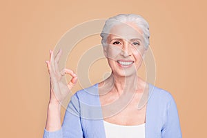 Close up portrait of happy elderly woman looking at the camera showing ok sign isolated on bright violet background