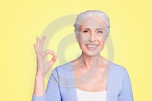 Close up portrait of happy elderly woman looking at the camera showing ok sign isolated on bright violet background