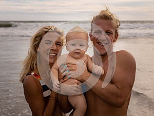 Close up portrait of happy family spending time on the beach. Father and mother holding infant baby boy. Smiling parents. Positive