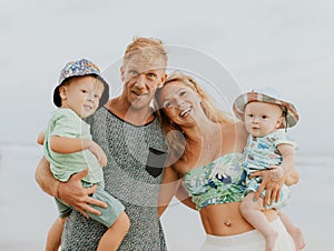 Close up portrait of happy family spending time on the beach. Father and mother holding sons. Cute baby boys. Smiling parents.