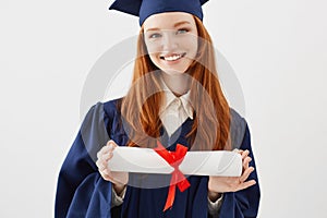 Close up portrait of happy foxy girl graduate in cap smiling holding diploma. Young redhead woman student future lawyer