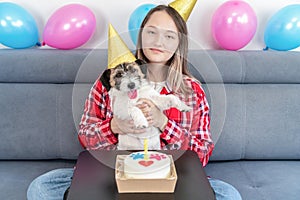 Close-up Portrait of a happy girl with her funny pet dog Jack Russell Terrier dog celebrating her birthday at home. Design by cake