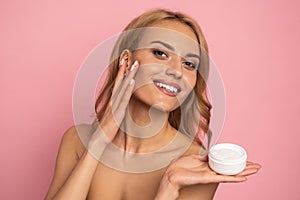 Close up portrait of happy gorgeous smiling attractive satisfied young woman with beaming smile, she is holding a cream jar and