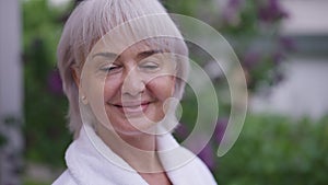 Close-up portrait happy grey-haired middle aged woman with brown eyes smiling looking at camera standing outdoors