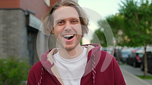 Close-up portrait of happy handsome young hipster man, guy standing outdoors street alone smiling and laughing looking